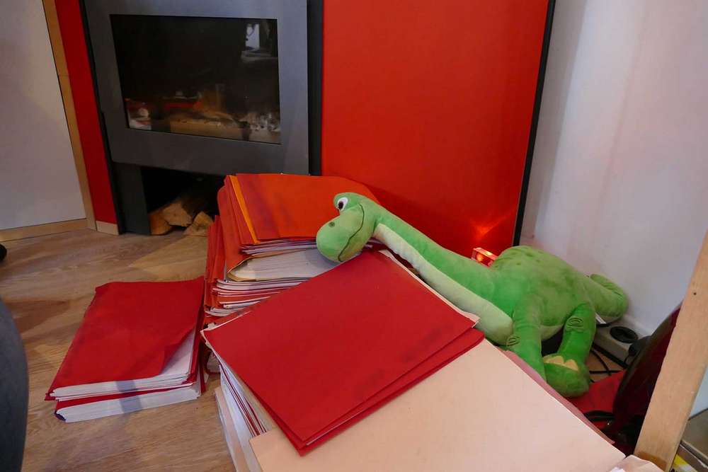 Plusieurs piles de dossiers rouges et orange dans le bureau d’un avocat qui fait du pro deo à Namur. Une cheminée dans le fond. Une peluche dinosaure parmi les dossiers.