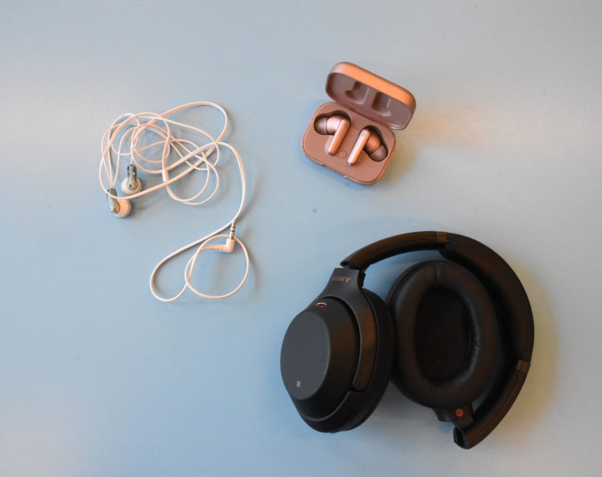 Vue aérienne de plusieurs types d'écouteurs posés sur une table : filaires, Bluetooth, casque Bluetooth.